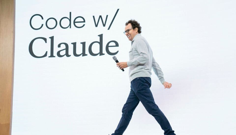 En mann går forbi en lysvegg med teksten Code w/ Claude