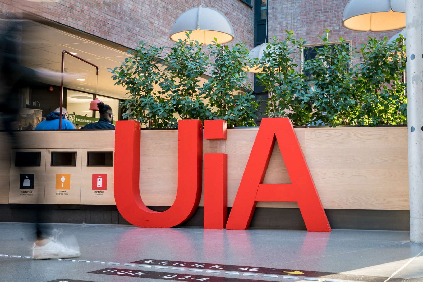 UiA-logoen i røde bokstaver på campus ved Universitetet i Agder